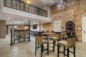 A hotel lobby with a brick wall, a chandelier, a staircase, and a reception desk.