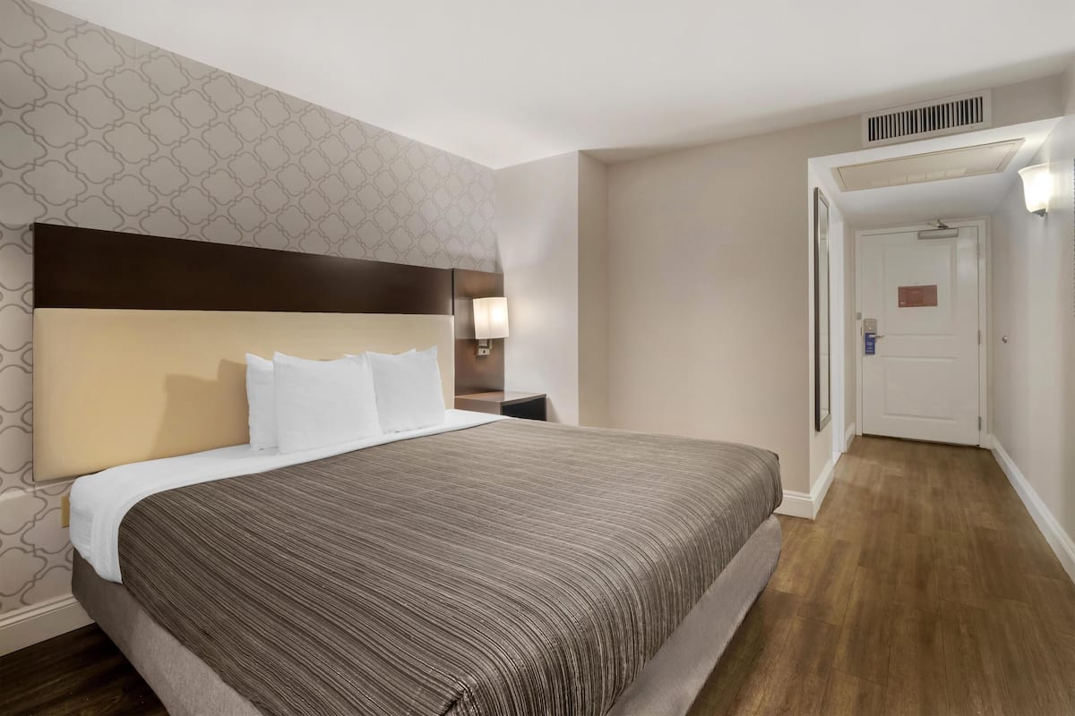 Hotellihuone, jossa on suuri sänky, pääty, yöpöytä ja seinään kiinnitetty lamppu.
