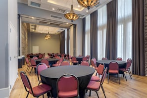 A conference room with round tables and chairs, large windows with curtains, and a chandelier.