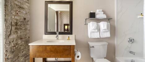 A bathroom with a brick wall, a sink with a mirror, a toilet, a shower, and a towel rack.