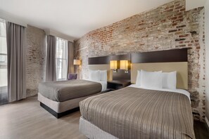 Une chambre d’hôtel avec deux lits, un mur en briques et une grande fenêtre avec des rideaux.
