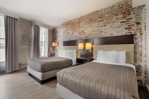 Habitación de hotel con dos camas, una pared de ladrillo y un ventanal con cortinas.