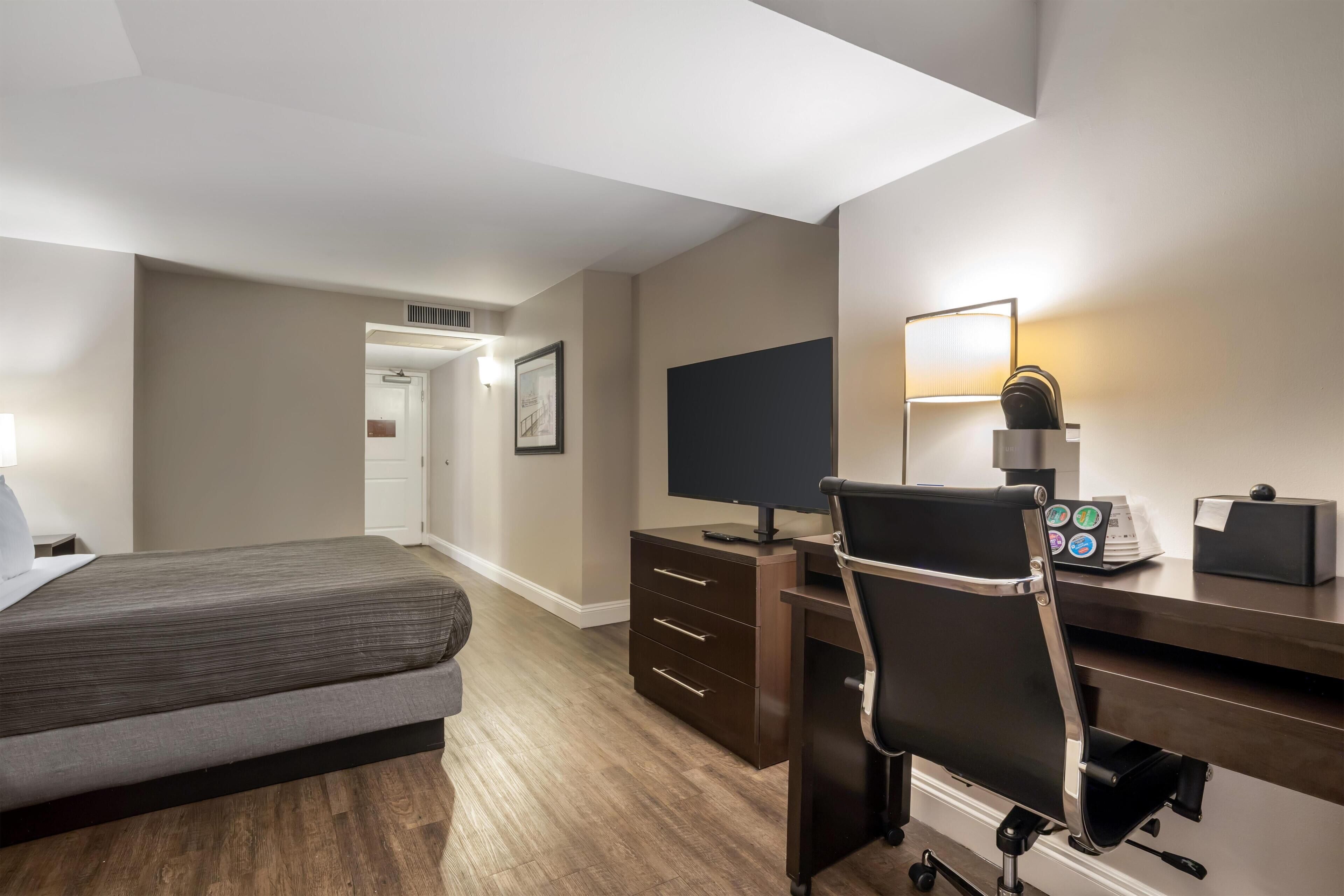 Habitación de hotel con cama, escritorio, silla, televisor y lámpara.