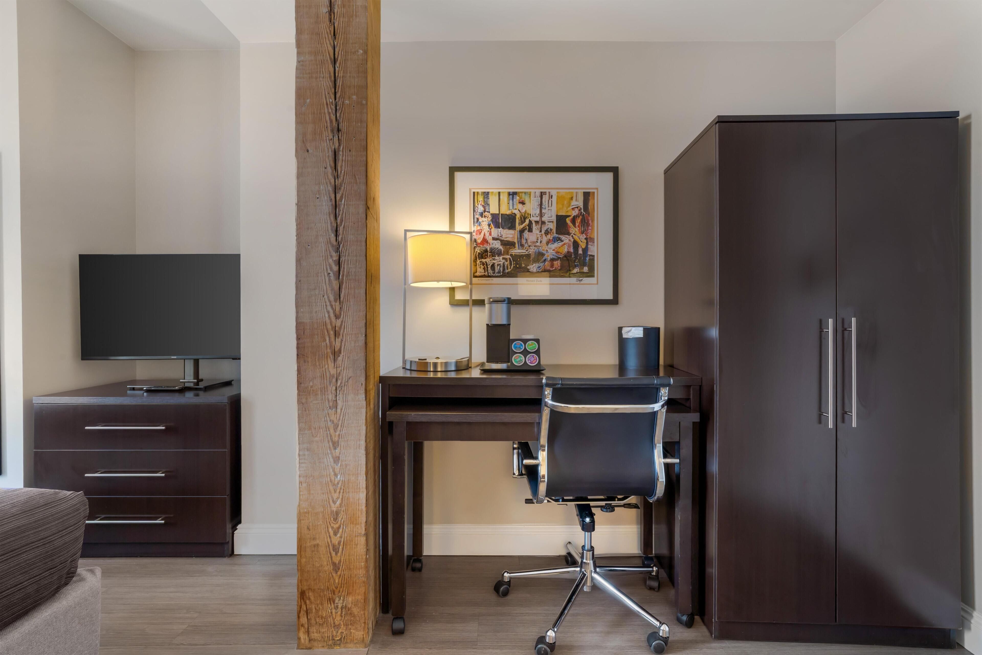 Una habitación de hotel con escritorio, silla, armario, televisión y una obra de arte en la pared.