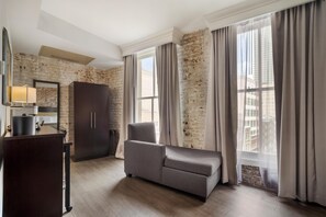 Une pièce comprenant un canapé, un meuble, une lampe et offrant une vue sur les bâtiments à travers de grandes fenêtres.