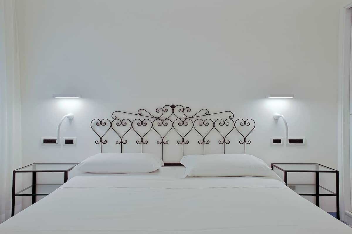 A bed with a metal headboard, two bedside tables, and wall-mounted reading lamps.