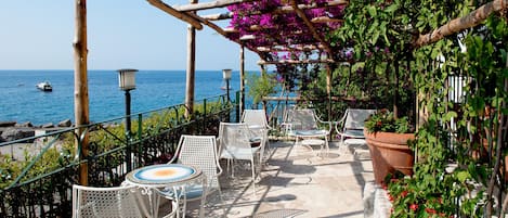 A terrace with white metal chairs and tables, overlooking the sea.