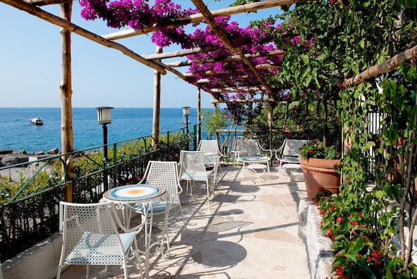 Une terrasse dotée de chaises et de tables en métal blanc, offrant une vue sur la mer.