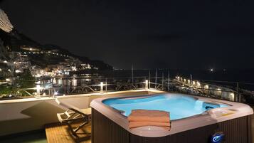 Un jacuzzi en un balcón con vistas a un pueblo costero de noche.
