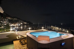 Un jacuzzi en un balcón con vistas a un pueblo costero de noche.