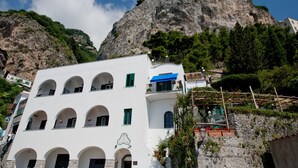 A white building with multiple arches and balconies, situated in a mountainous area with a rocky cliff in the background. - Hotel Aurora (Amalfi)