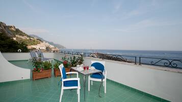 Um terraço com mesa e cadeiras, plantas em vasos e vista para o mar e edifícios.