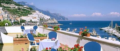 A terrace with tables and chairs overlooking a marina and coastal town.