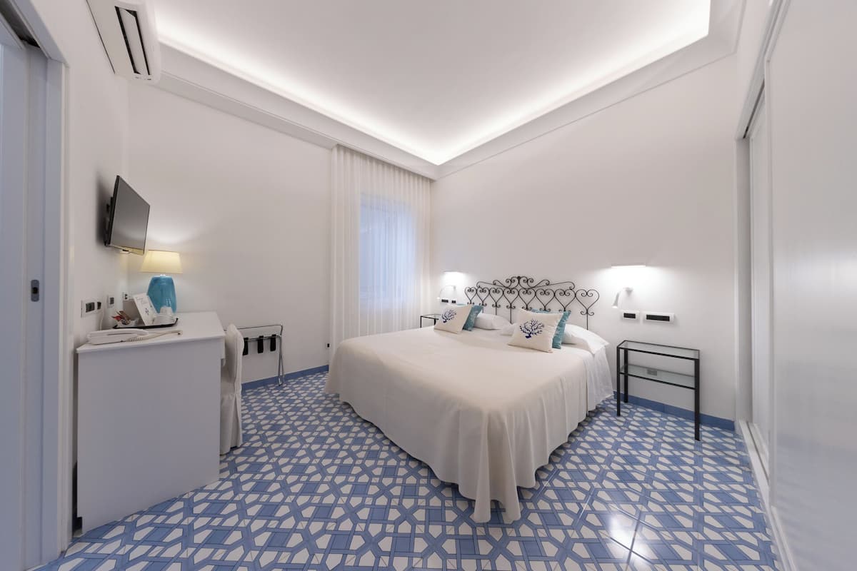 A hotel room with a bed, bedside tables, a desk, and a TV.