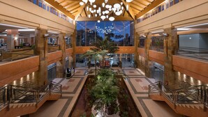 Un atrium à plusieurs niveaux, doté d’un élément décoratif central en eau, de poutres en bois et d’un lustre moderne.