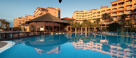 Un hotel con piscina, palmeras y una estructura con techo de paja.