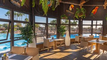 Un restaurante con amplios ventanales que dan a una piscina, muebles de mimbre y decoración tropical.