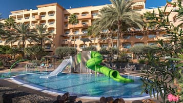 Relax by the pool surrounded by lush palm trees and tropical plants, with a fun water slide for a refreshing dip.