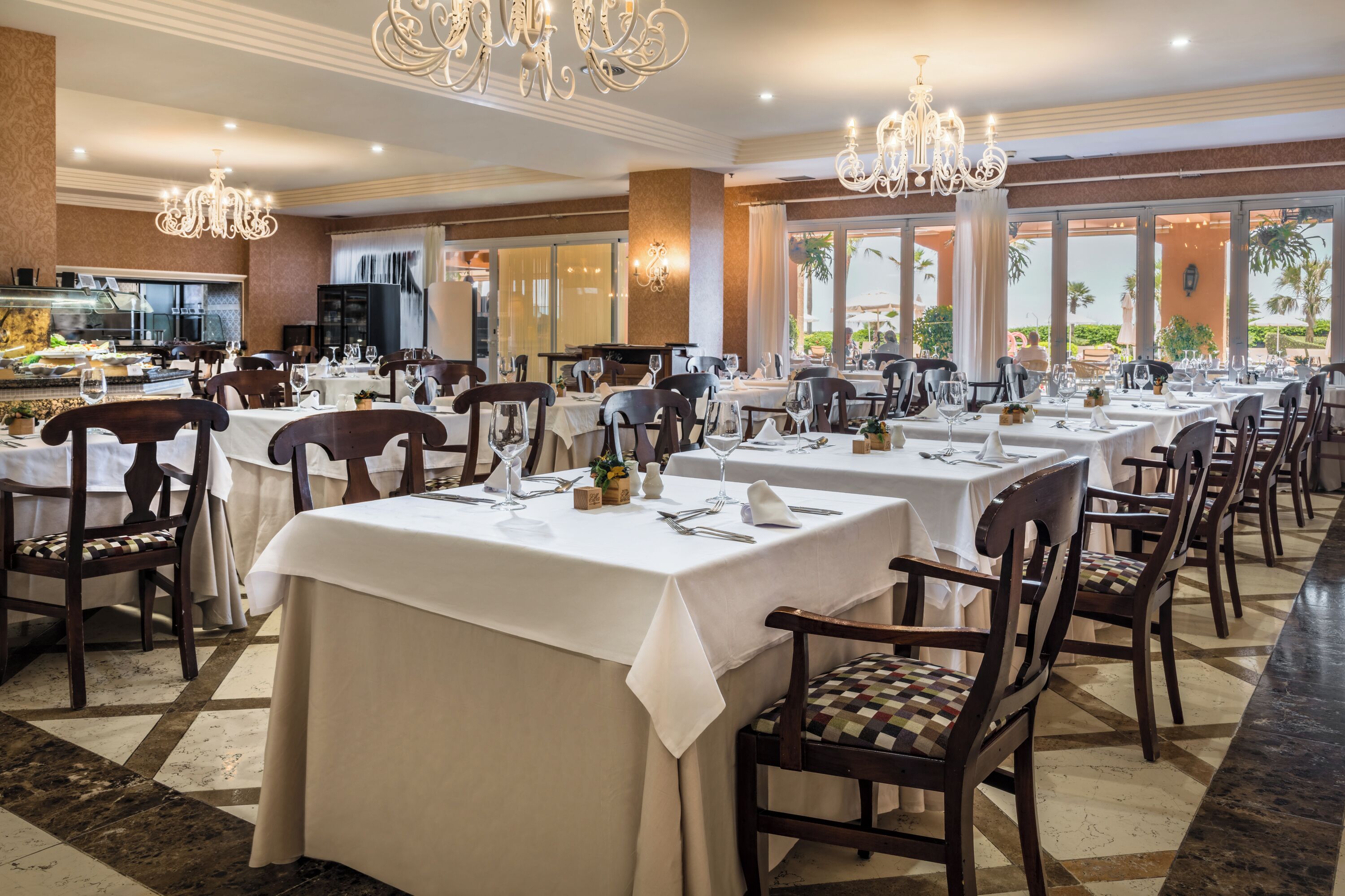A restaurant with multiple tables and chairs, chandeliers, and a view of the outdoors.