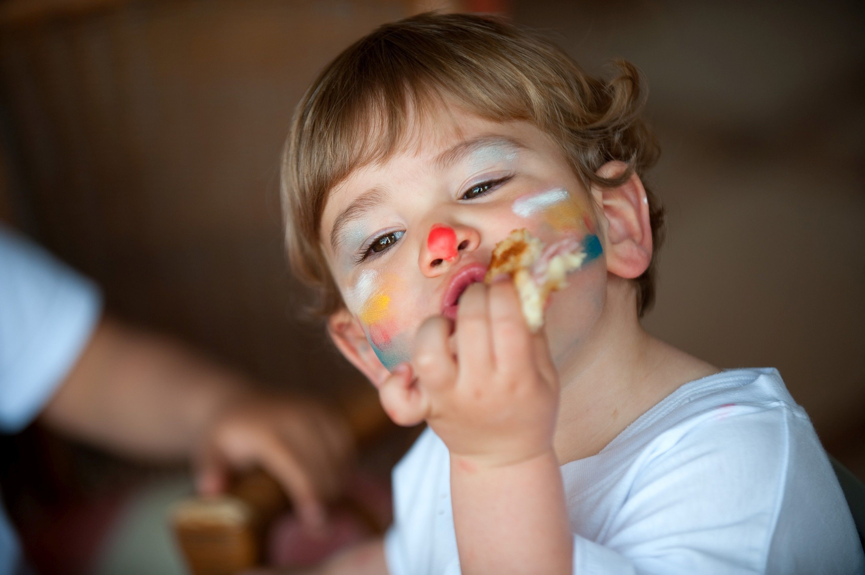 Un niño con pintura de cara colorida, usando una camisa blanca, en una habitación con pared de madera.
