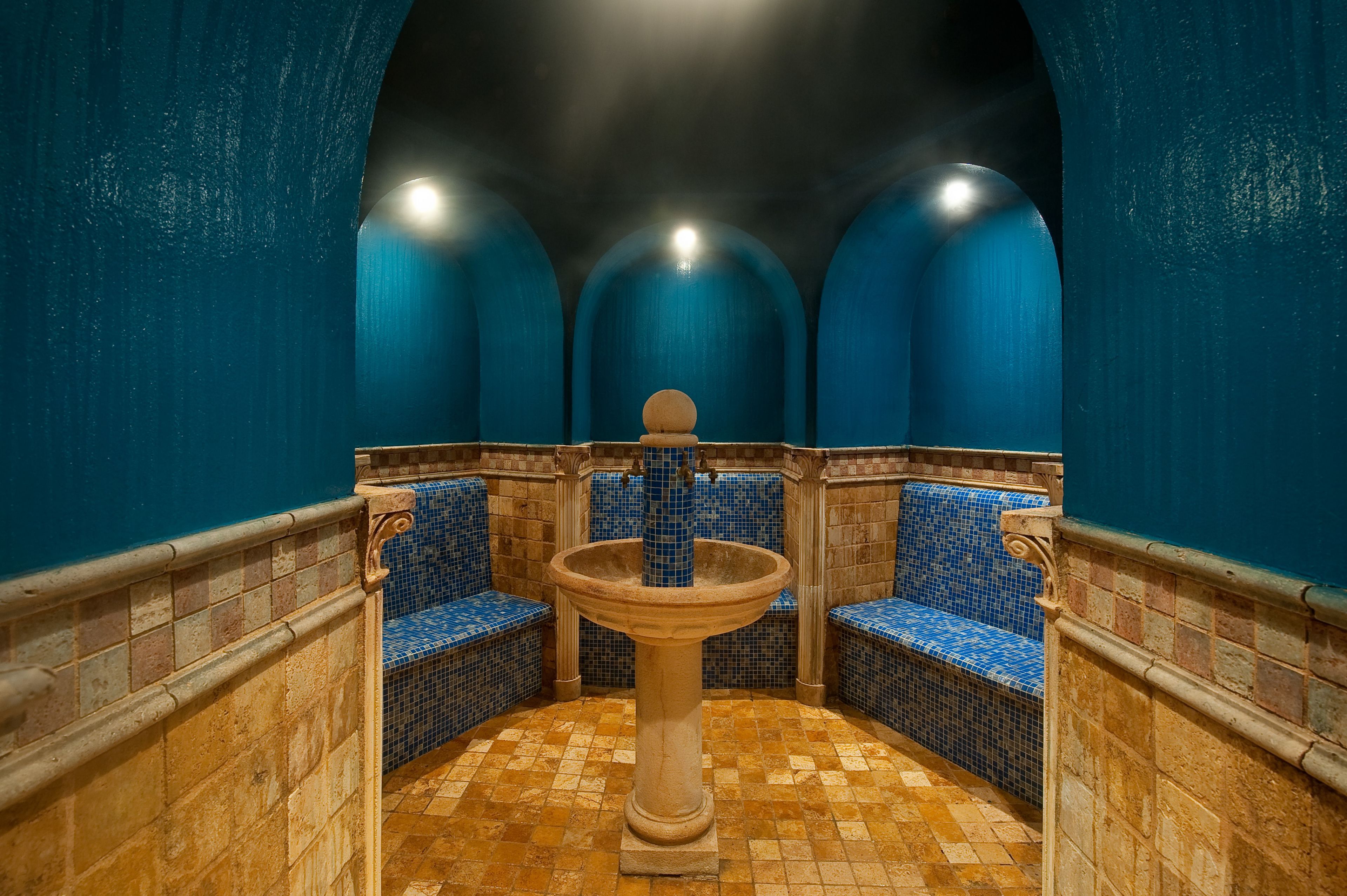 A bathroom with blue tiled walls, a central sink, and two blue-tiled benches.