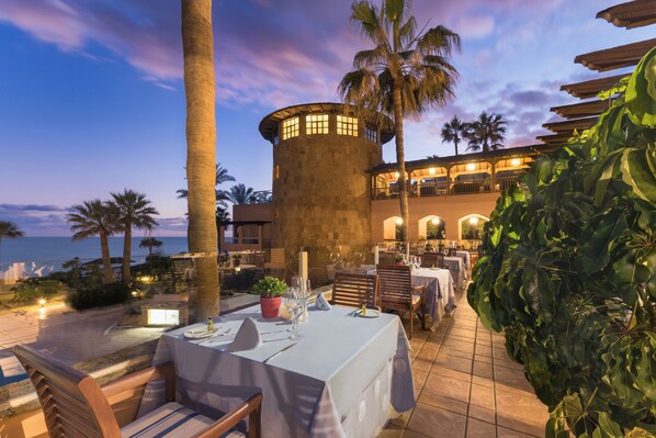Un restaurante con terraza, una torre de piedra y vista al océano.