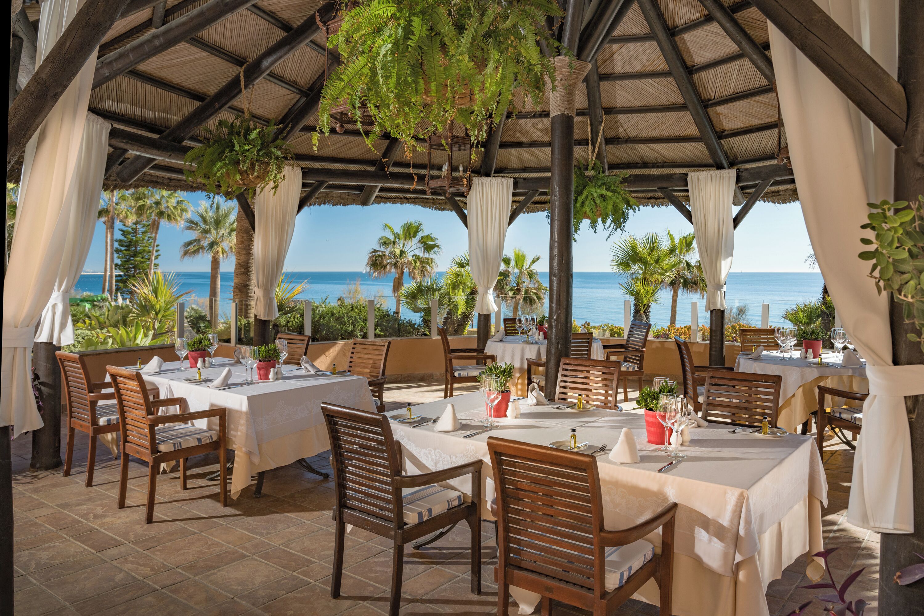 A seaside restaurant with tables set for dining, overlooking the ocean.