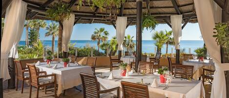 A seaside restaurant with tables set for dining, overlooking the ocean.