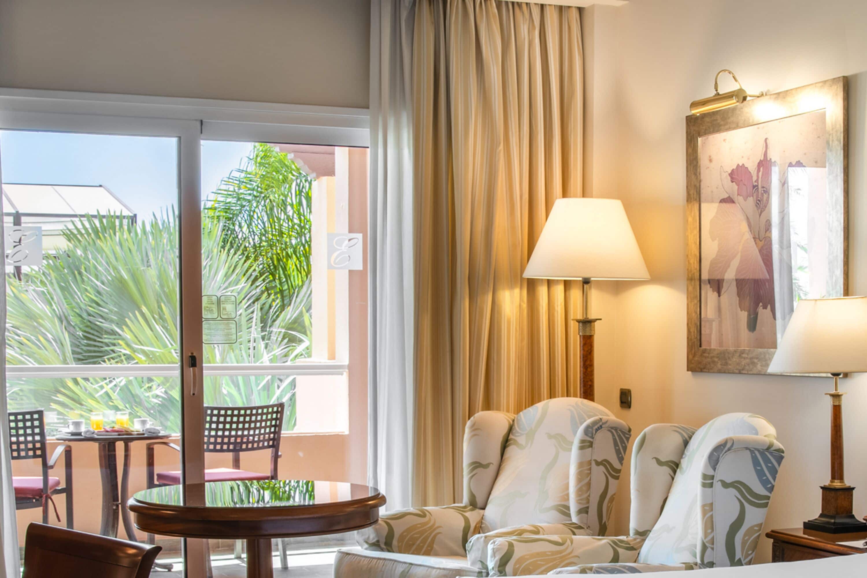 Een hotelkamer met balkon, een tafel met stoelen, een bank en een lamp.