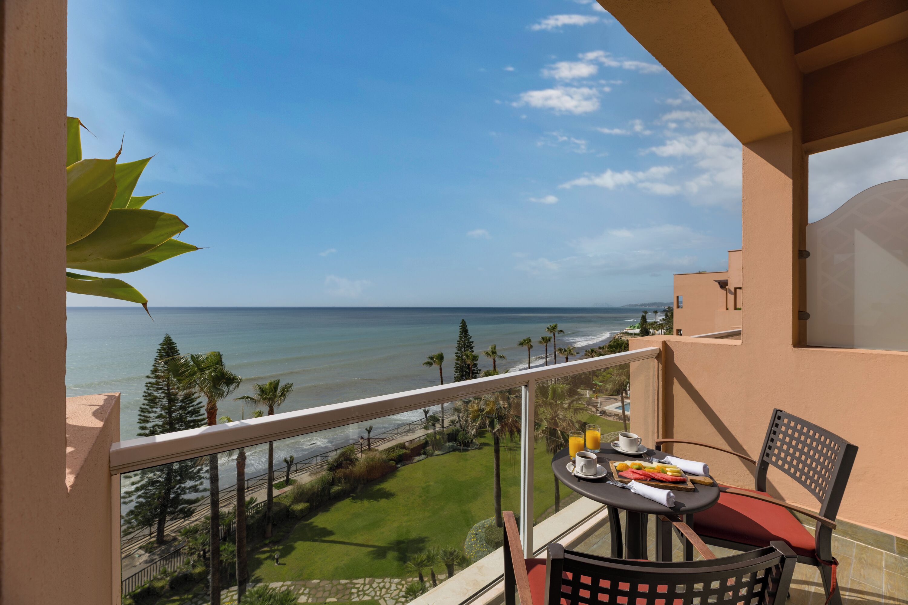 Un balcón con una mesa dispuesta para el desayuno, con vista a una playa y al océano.