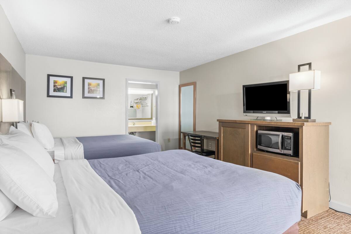 A hotel room with two beds, a TV, a microwave, and a desk with a chair.