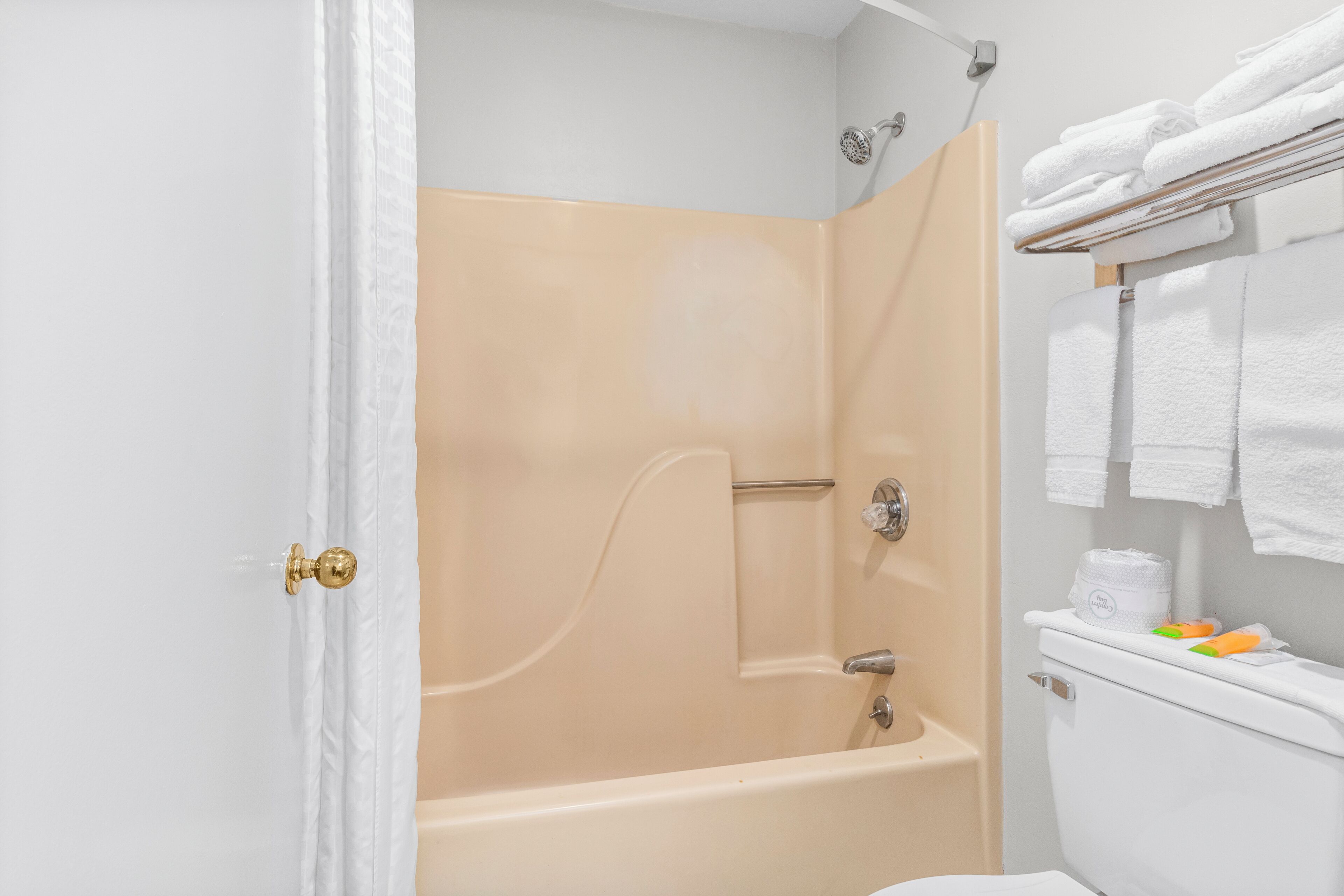 Un baño con box de ducha color beige, inodoro blanco y un perchero con toallas dobladas.