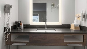 Un baño moderno con un espejo grande, un lavabo, un secador de pelo y una cafetera.