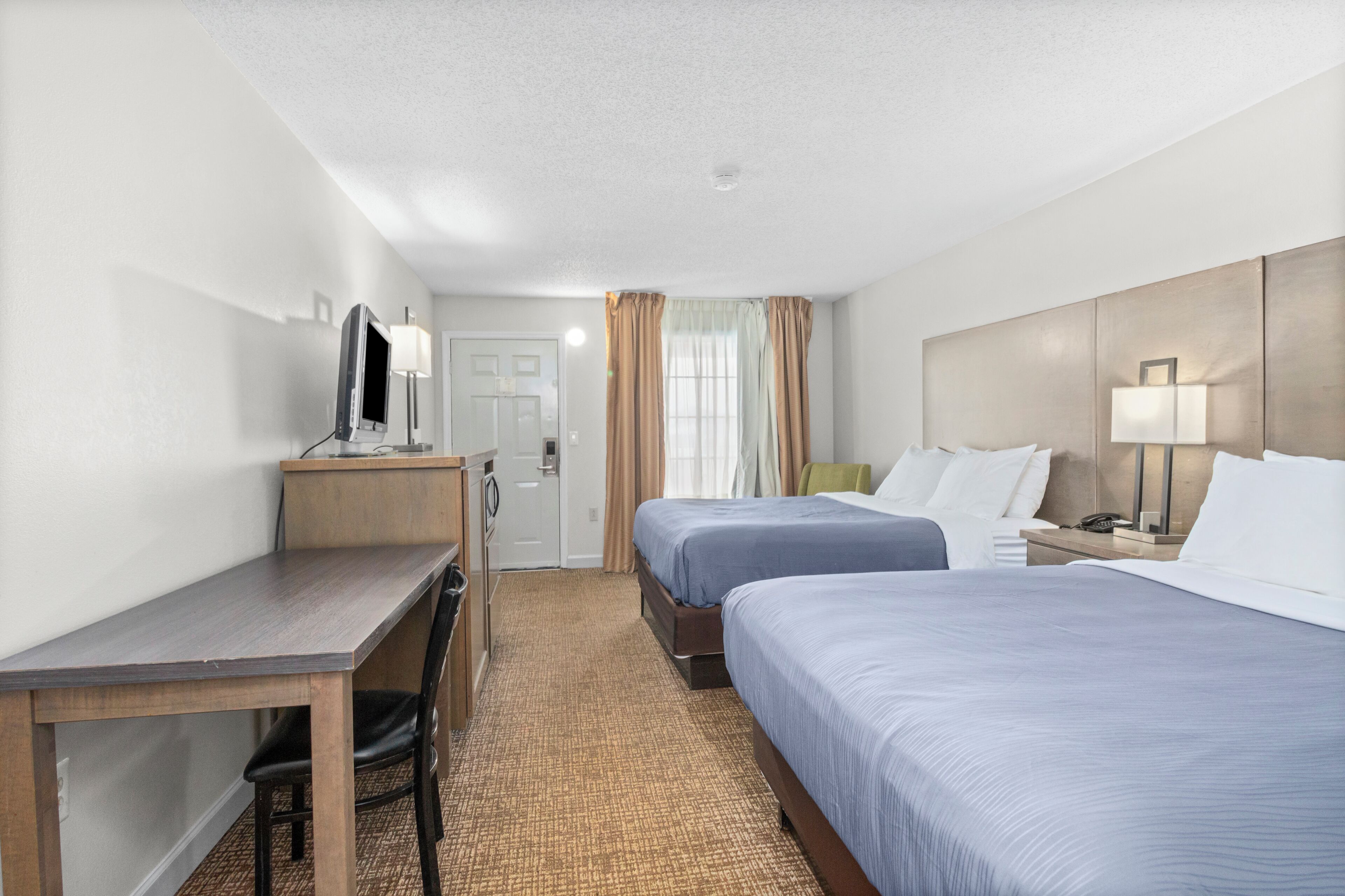 Une chambre d’hôtel avec deux lits, un bureau, une chaise, une télévision et une salle de bain.