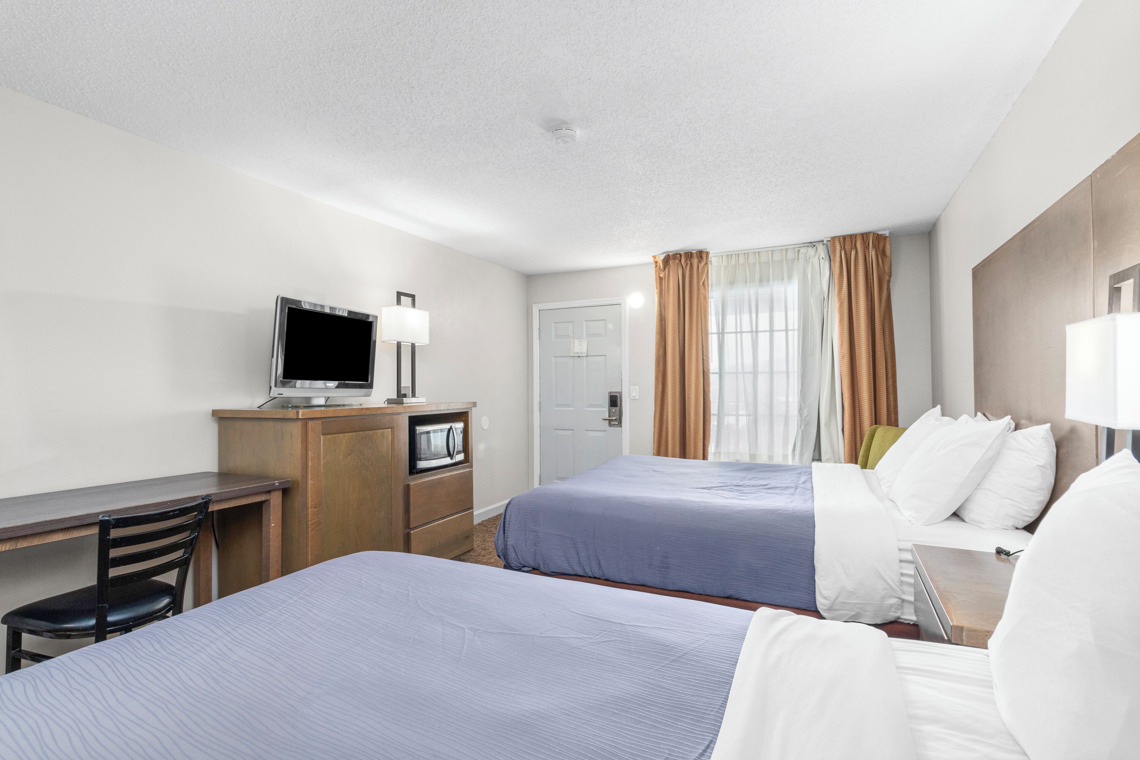 Une chambre d’hôtel avec deux lits, un bureau avec une télévision, un minibar et une porte.