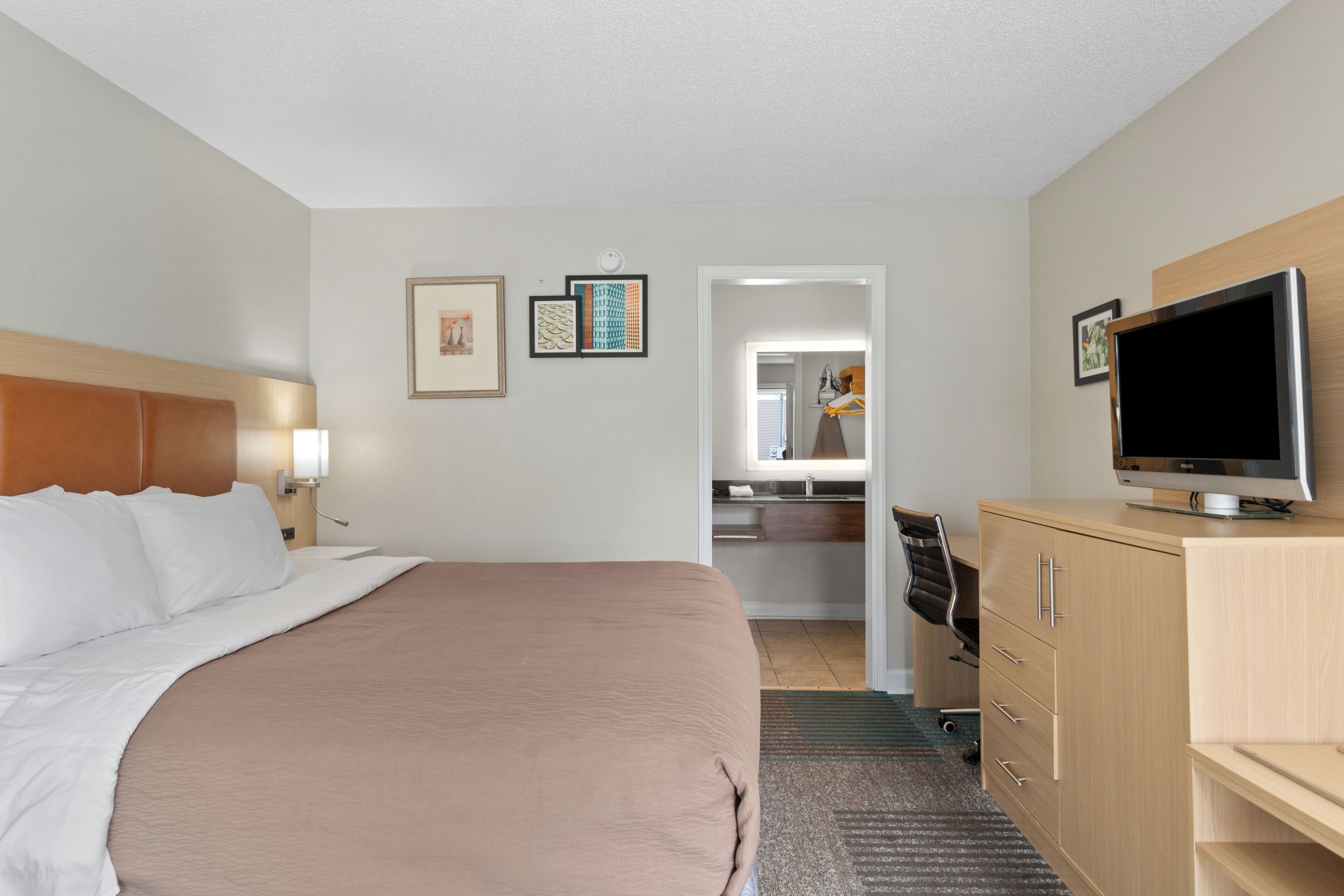 Habitación de hotel con cama, televisor, escritorio con silla y baño visible a través de una puerta abierta.