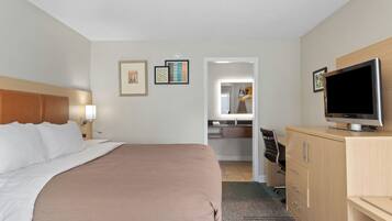 Habitación de hotel con cama, televisor, escritorio con silla y baño visible a través de una puerta abierta.