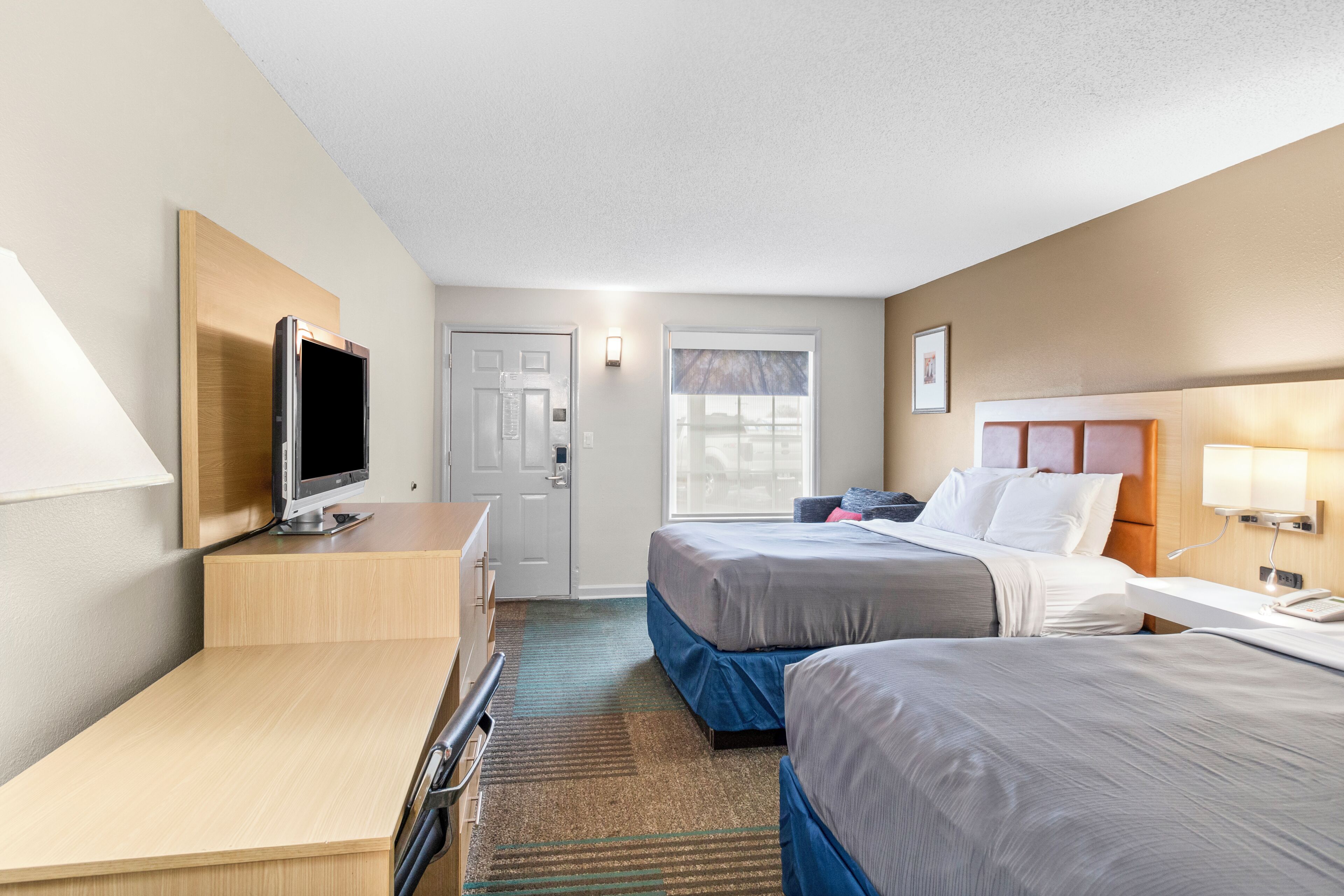 Een hotelkamer met twee bedden, een bureau, een televisie en een deur.
