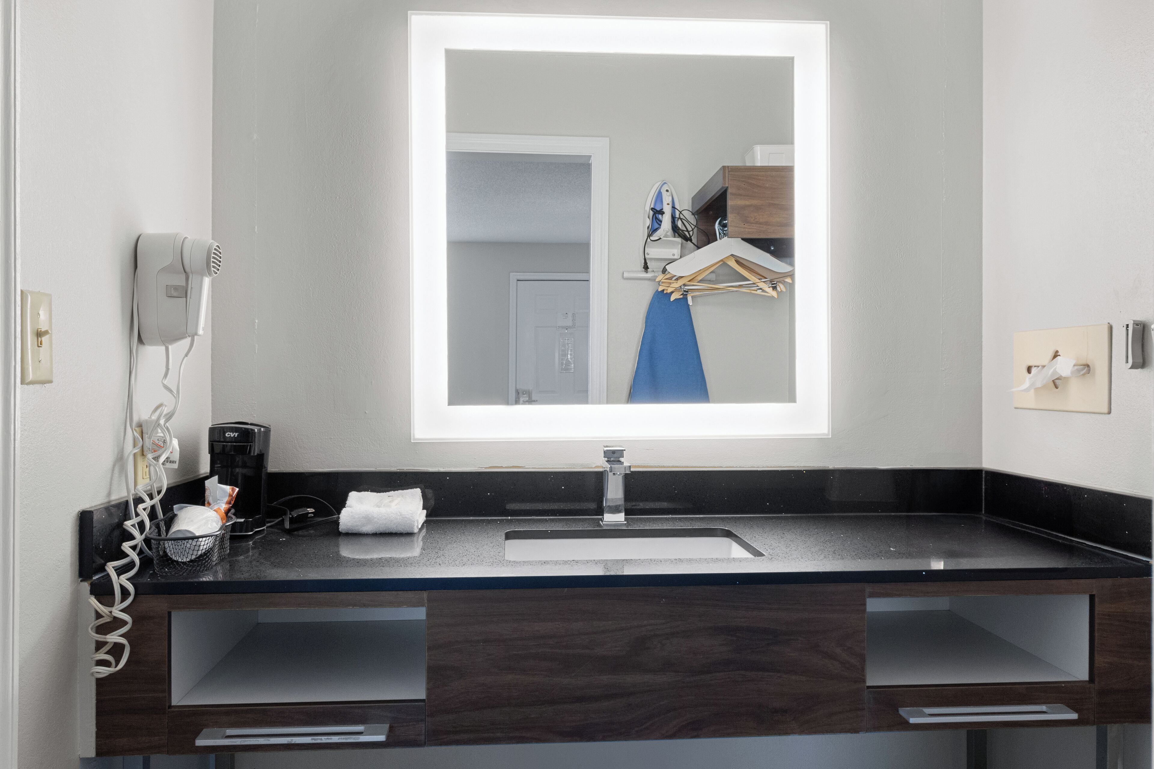Un baño con un espejo grande, un lavabo, un secador de pelo y un perchero para toallas.