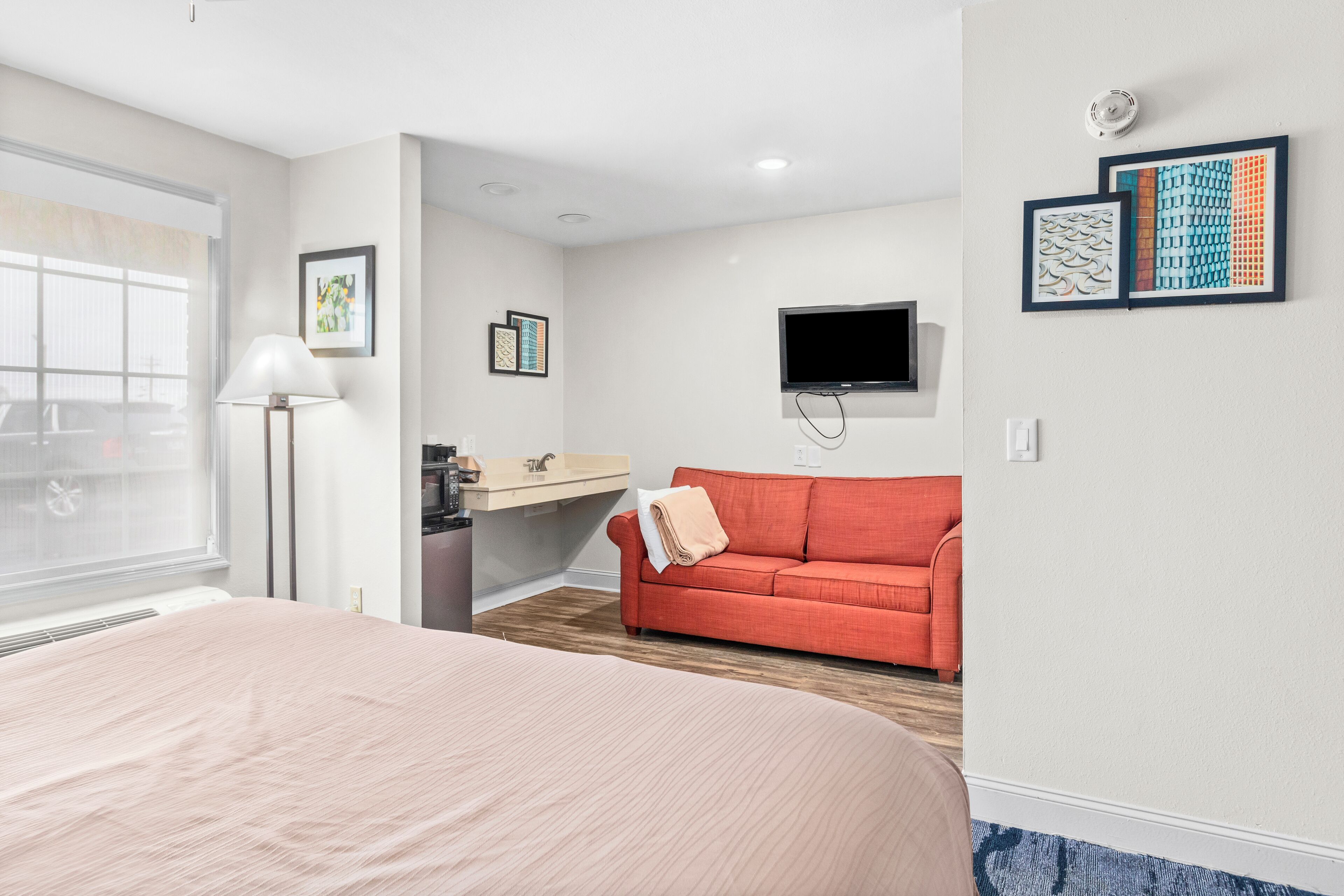 A hotel room with a bed, a red sofa, a TV, and artwork on the walls.
