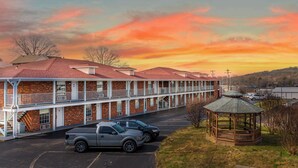 Un motel con una estructura de dos pisos, un porche cubierto y un estacionamiento.