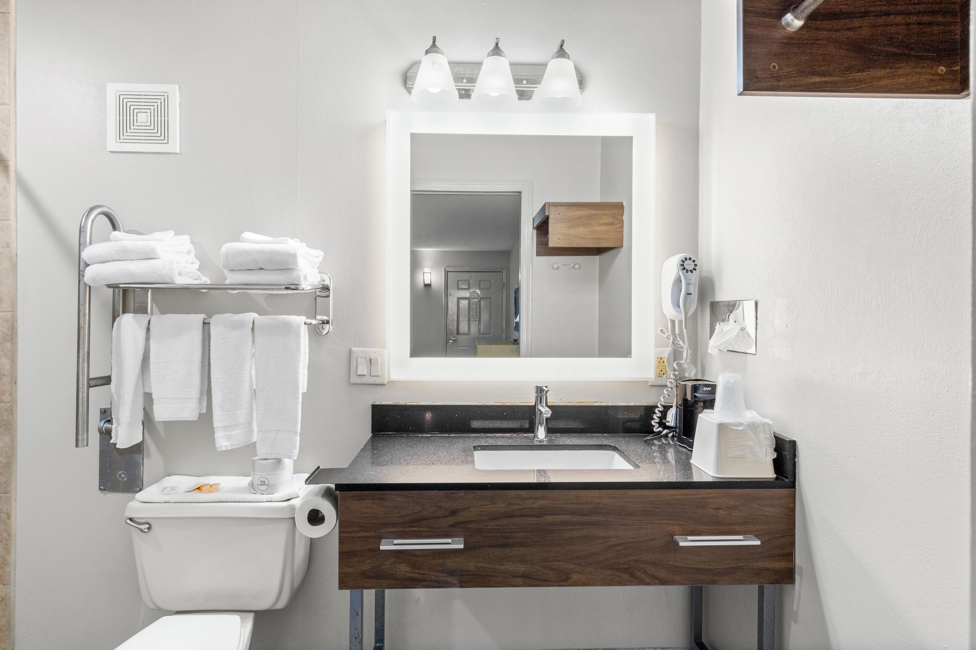 A modern bathroom with a white toilet, a sink with a mirror above it, and a towel rack with folded towels.