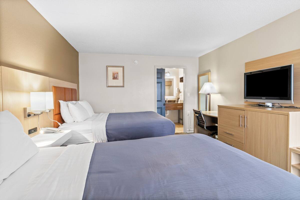 A hotel room with two beds, a television, a desk with a lamp, and a bathroom visible through an open door.