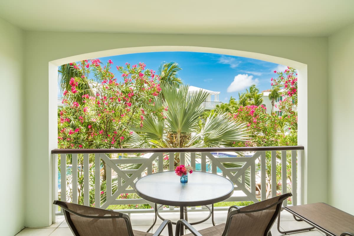 Een balkon met een ronde tafel en stoelen, omgeven door witte hekken en weelderige begroeiing.