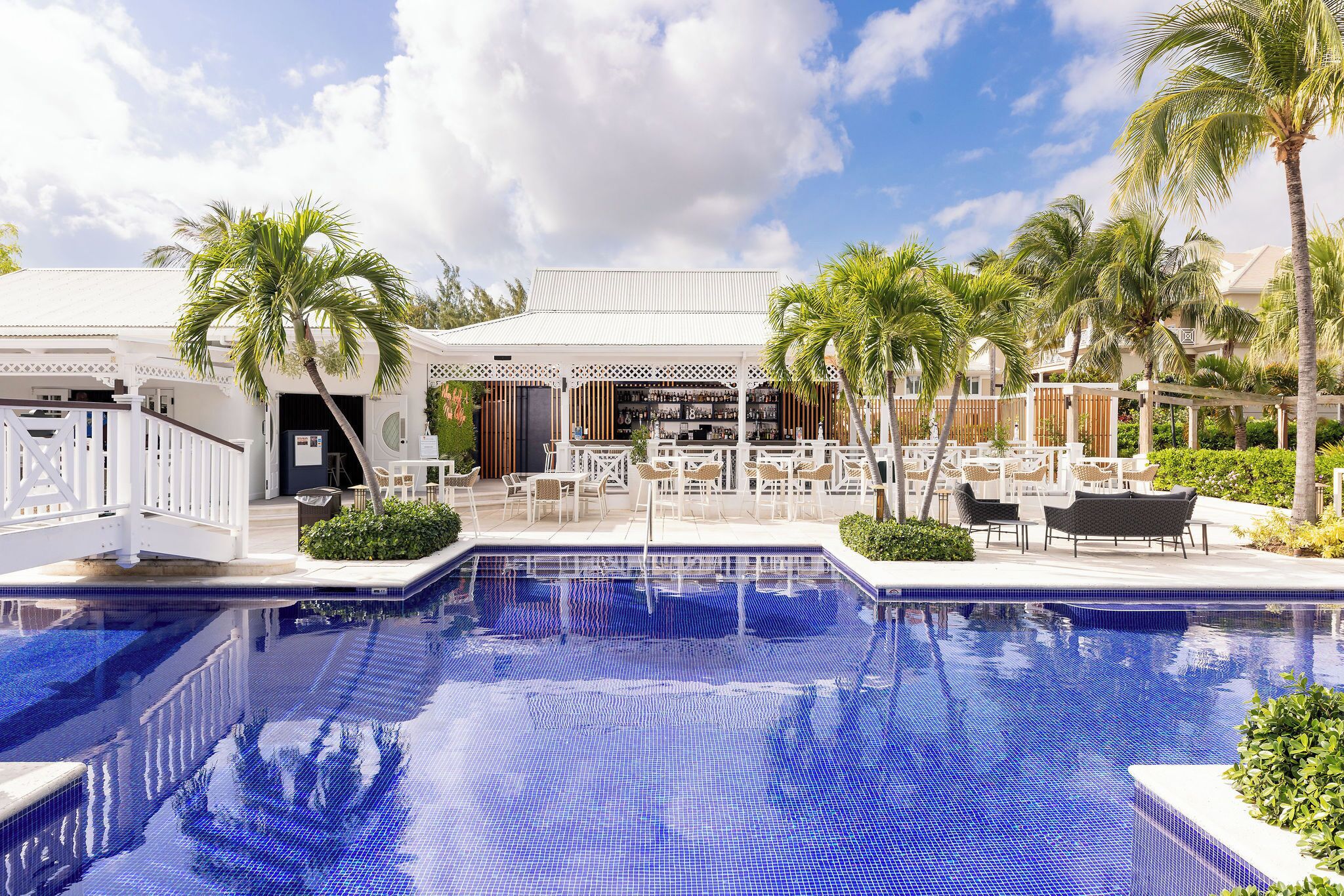 A pool area with a tiled pool, lounge chairs, and palm trees.