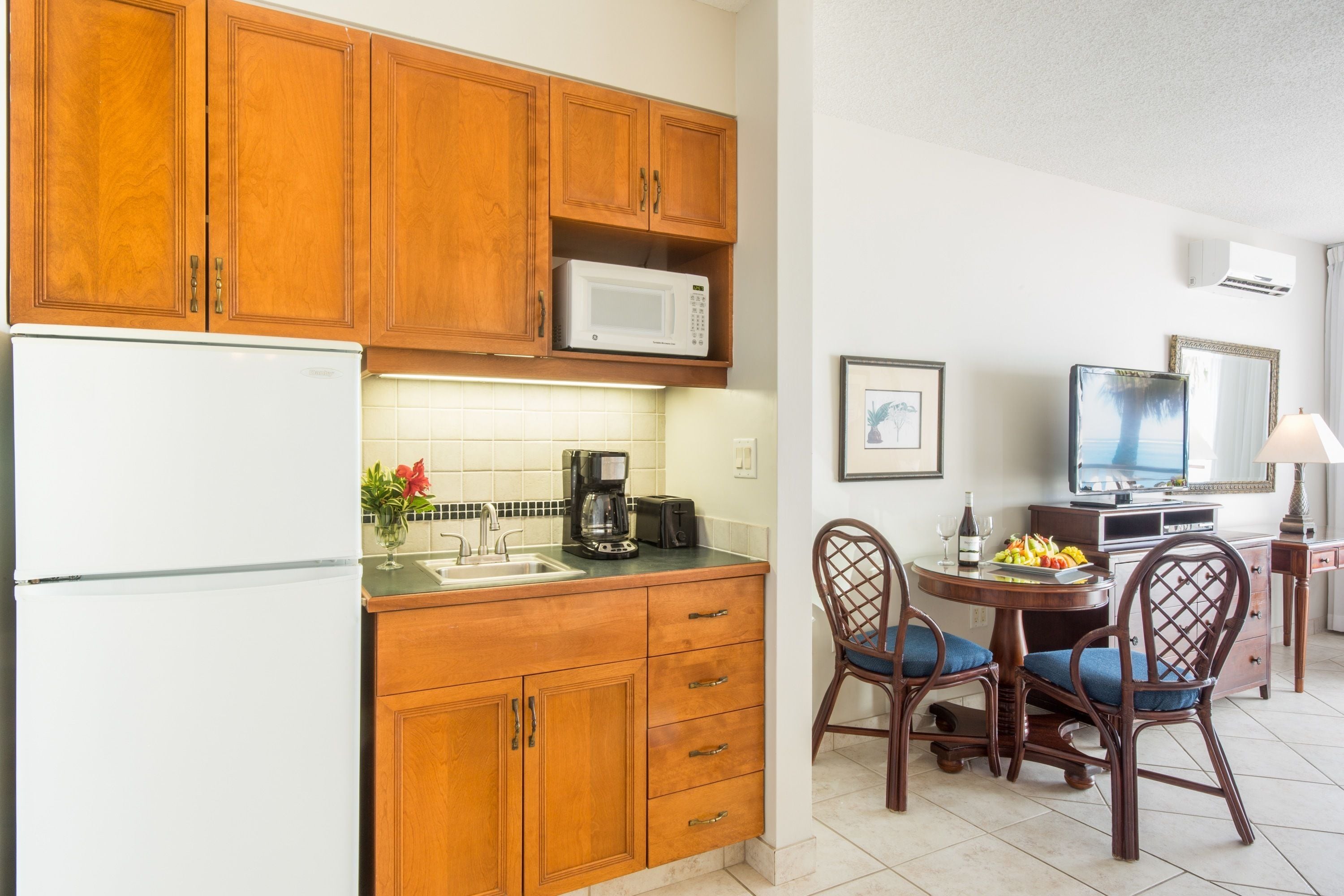 A compact kitchen with wooden cabinets, a microwave, a coffee maker, and a dining area with two chairs and a small table.