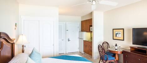 A hotel room with a bed, a desk with a television, a dining area, and a kitchen.