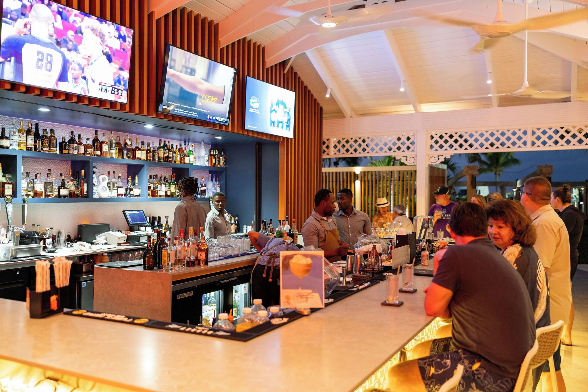 A bar area with multiple TVs, a well-stocked liquor shelf, and a counter with bar tools.
