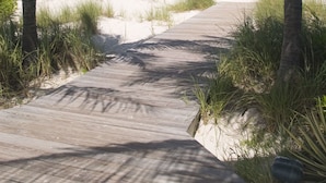 Un sentier en bois mène à une plage où l’eau est d’un bleu turquoise cristallin et où poussent des palmiers.