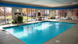 An indoor swimming pool with clear water, surrounded by windows, potted plants, and a lifeguard sign. - Crossroads Inn And Suites (Salem)